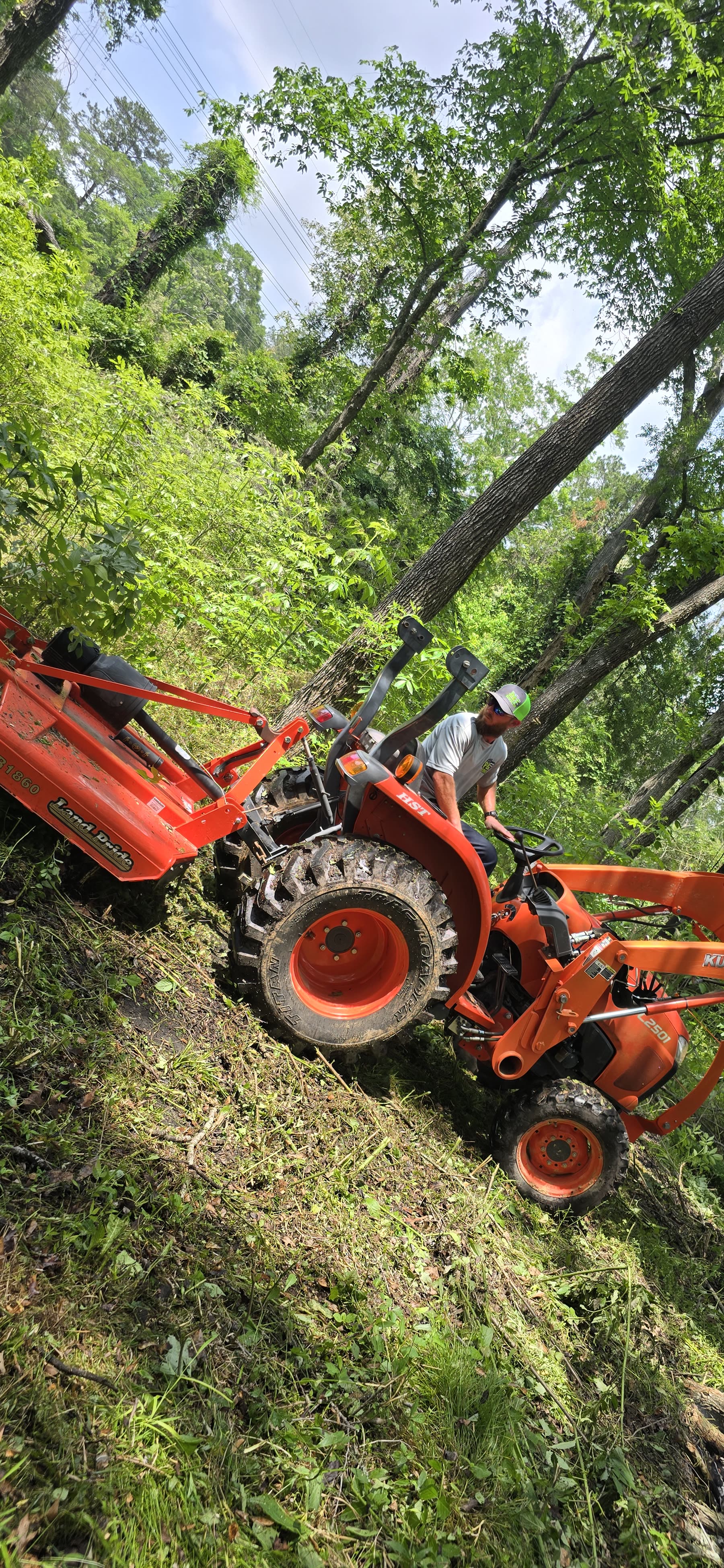 Orange Kubota tractor clearing heavy brush on a wooded lot in Liberty County